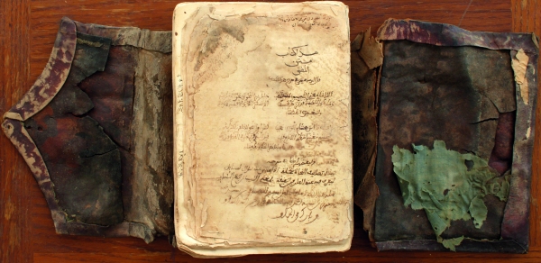 Un vieux livre patiné avec une écriture arabe, ses couvertures endommagées et décolorées faisant allusion à un passé historique dans les bibliothèques de Tombouctou, où résident de précieux manuscrits du Mali.